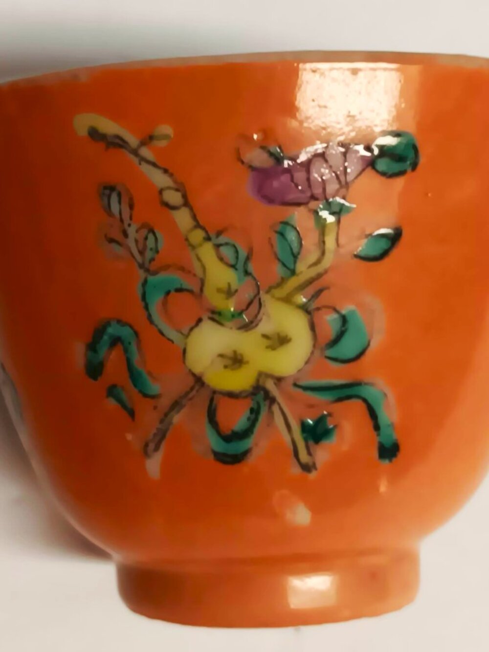 Antique Chinese coral ground teacup with enameled emblems and ribbons.